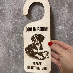 以下が含まれることがあります： 犬の白黒イラストが描かれた木製ドアハンガー。ハンガーのテキストは「Dog in Room! Please Do Not Disturb!」です