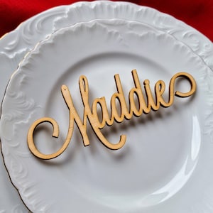 May include: A white ceramic plate with a wooden name card that reads "Maddie".