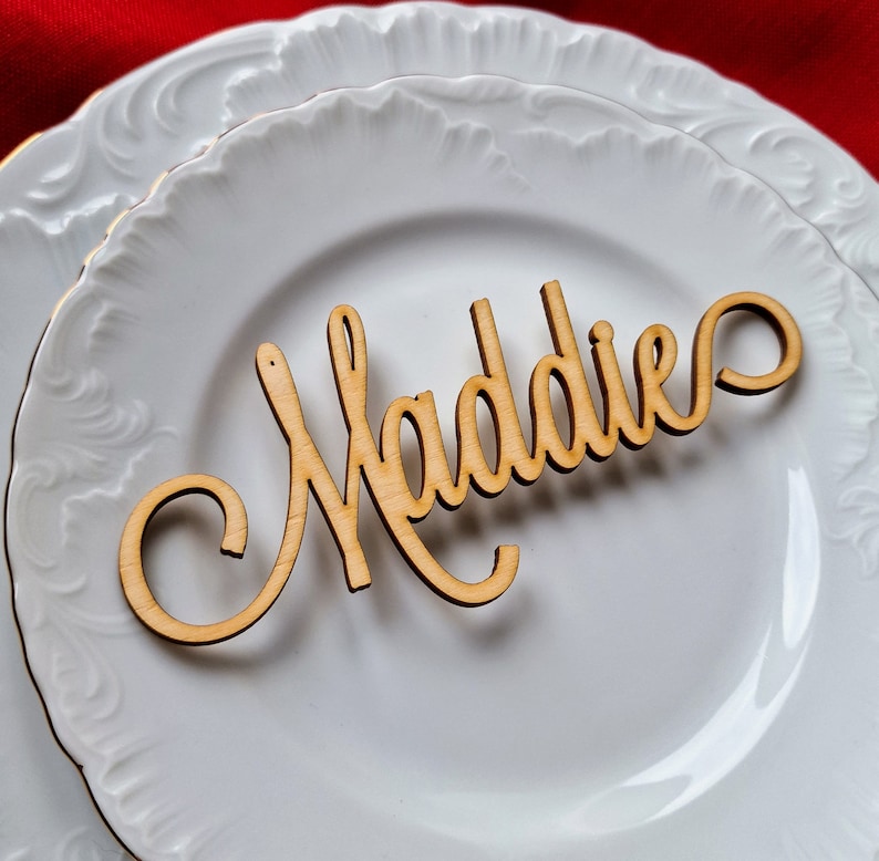 May include: A white ceramic plate with a wooden name card that reads "Maddie".