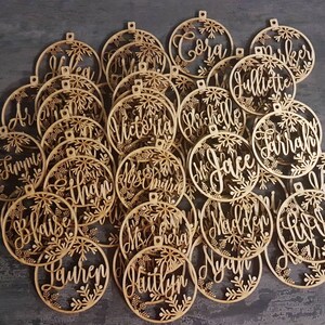 May include: A collection of wooden ornaments with snowflake designs and personalized names, including "Cora", "Farrah", "Lauren", "Faith", and "Blaise".