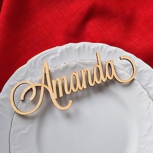 May include: A wooden place card with the name "Amanda" written in a cursive font. The place card is on a white plate with a gold rim.
