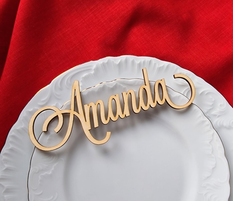 May include: A wooden place card with the name "Amanda" written in a cursive font. The place card is on a white plate with a gold rim.