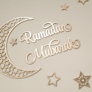 May include: Wooden cutout of a crescent moon with an intricate geometric pattern, along with the words "Ramadan Mubarak" and several stars.