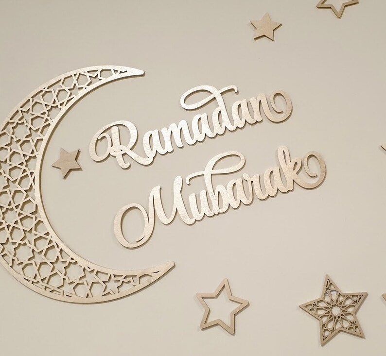 May include: Wooden cutout of a crescent moon with an intricate geometric pattern, along with the words "Ramadan Mubarak" and several stars.