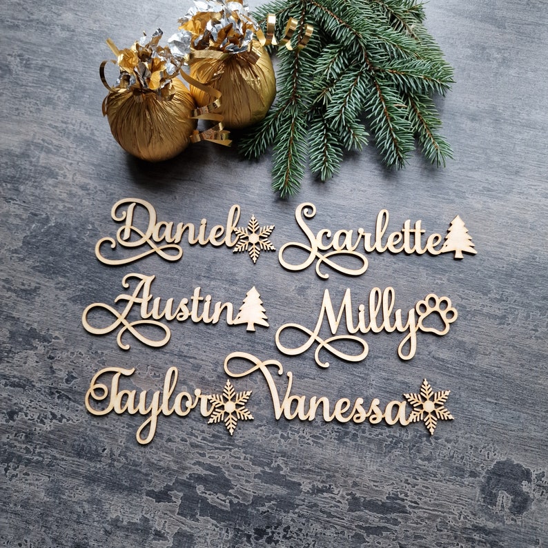 May include: Wooden Christmas ornaments with names "Daniel", "Scarlette", "Austin", "Milly", "Taylor", and "Vanessa" with various holiday-themed decorations.