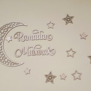 May include: Wooden cutout of a crescent moon with an intricate design, surrounded by stars. The words "Ramadan Mubarak" are written in cursive script.