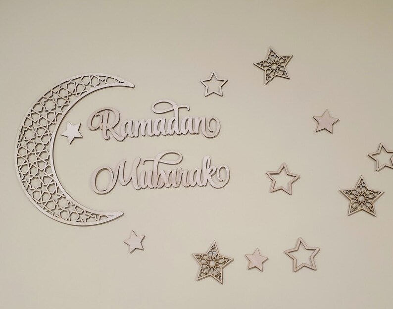 May include: Wooden cutout of a crescent moon with an intricate design, surrounded by stars. The words "Ramadan Mubarak" are written in cursive script.