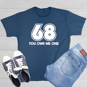 May include: A navy blue t-shirt with white text that says "68 You Owe Me One". The number 68 is in a large, bold font.