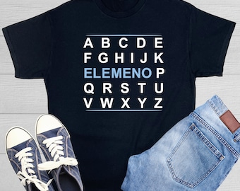 Può includere: Maglietta nera con un design alfabetico bianco. La lettera "E" è evidenziata in blu. La maglietta è abbinata a jeans blu e scarpe da ginnastica nere.