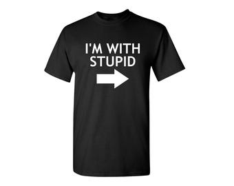 May include: A black short-sleeved t-shirt featuring the white text I'M WITH STUPID printed on the chest, positioned above a white horizontal arrow pointing toward the right side of the garment.