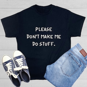 May include: A black t-shirt with the text "PLEASE DON'T MAKE ME DO STUFF" in white. The shirt is paired with blue jeans and navy blue sneakers with white laces, creating a casual outfit.