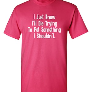 May include: Pink t-shirt with white text that reads "I Just Know I'll Die Trying To Pet Something I Shouldn't."