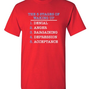 May include: Red t-shirt with white text that reads "THE 5 STAGES OF WAKING UP" and a list of the stages: 1. Denial, 2. Anger, 3. Bargaining, 4. Depression, 5. Acceptance.