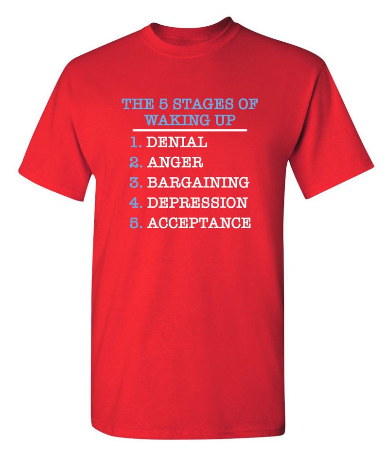 May include: Red t-shirt with white text that reads "THE 5 STAGES OF WAKING UP" and a list of the stages: 1. Denial, 2. Anger, 3. Bargaining, 4. Depression, 5. Acceptance.