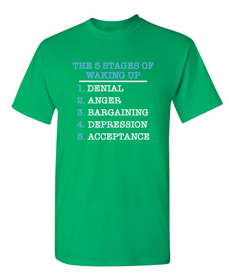 May include: Green t-shirt with white text that reads "The 5 Stages of Waking Up" and lists the stages as: 1. Denial, 2. Anger, 3. Bargaining, 4. Depression, 5. Acceptance.