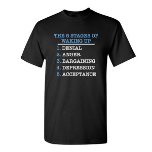 May include: Black t-shirt with white text that reads "THE 5 STAGES OF WAKING UP" and a list of the stages: Denial, Anger, Bargaining, Depression, Acceptance.