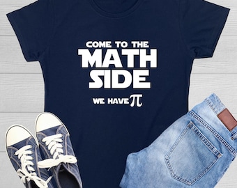 May include: A navy blue short-sleeved t-shirt featuring the white text "COME TO THE MATH SIDE WE HAVE PI" with the pi symbol. The shirt is displayed alongside a pair of dark blue canvas sneakers with white laces and light blue denim jeans.