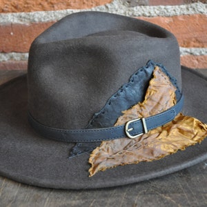 May include: A brown felt fedora hat with a black leather band and a brown leather leaf accent.