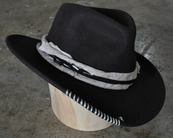 May include: A black felt cowboy hat with a white band and a black and white braided trim around the brim.