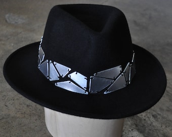 May include: A black fedora hat with a silver geometric band around the crown.