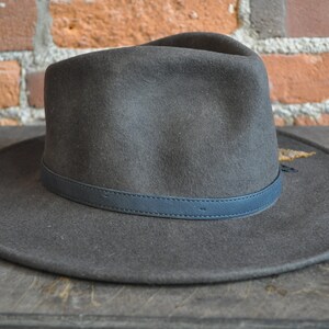 May include: A dark gray felt fedora hat with a dark blue leather band around the crown.