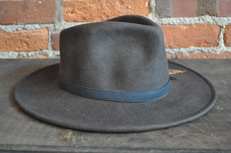 May include: A dark gray felt fedora hat with a dark blue leather band around the crown.