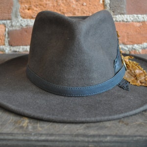 May include: A dark gray fedora hat with a black leather band and a brown feather accent.