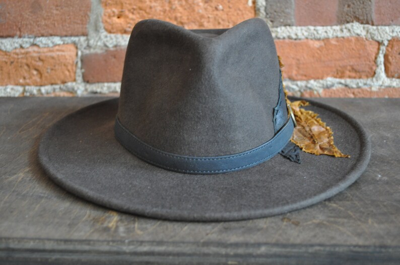 May include: A dark gray fedora hat with a black leather band and a brown feather accent.
