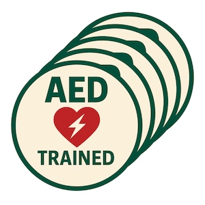 May include: A collection of cream-coloured, circular stickers with a dark green border. Each sticker displays the text "AED TRAINED" in dark green, with a red heart and lightning bolt graphic.