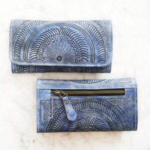 Puede incluir: Una cartera de cuero azul con un dise&ntilde;o estampado intrincado. La cartera tiene un cierre de cremallera y un cierre de solapa.