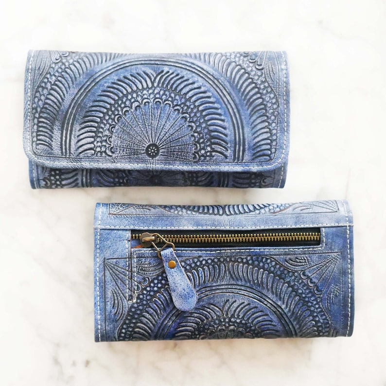 Puede incluir: Una cartera de cuero azul con un dise&ntilde;o estampado intrincado. La cartera tiene un cierre de cremallera y un cierre de solapa.