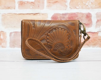 May include: A brown leather wallet with an intricate floral design and a matching strap. The wallet has a zipper closure and a metal clasp.