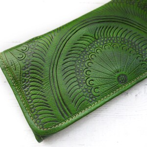 Puede incluir: Una cartera de cuero verde con un dise&ntilde;o estampado detallado. La cartera tiene un borde cosido y un cierre de solapa.