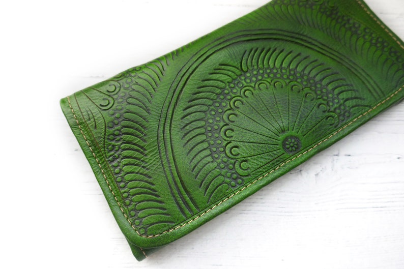 Puede incluir: Una cartera de cuero verde con un dise&ntilde;o estampado detallado. La cartera tiene un borde cosido y un cierre de solapa.
