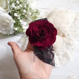 May include: A single, deep red rose with a black lace trim. The rose is on a white background.
