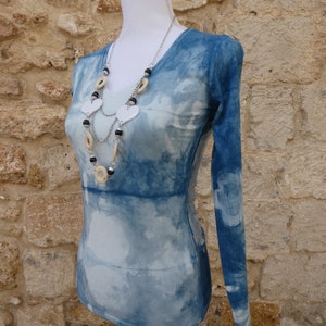 Può includere: Una camicia a maniche lunghe blu e bianca con stampa tie-dye con una collana di perline bianche e nere. La camicia è su un manichino bianco.