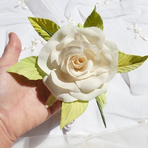 May include: A single white paper rose with green paper leaves. The rose is held in a hand.