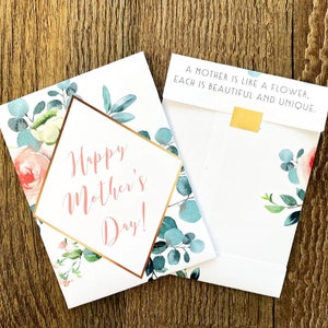 May include: Mother's Day greeting cards with floral designs. One card reads "Happy Mother's Day!" in pink script within a gold geometric frame. The other card reads "A mother is like a flower, each is beautiful and unique."