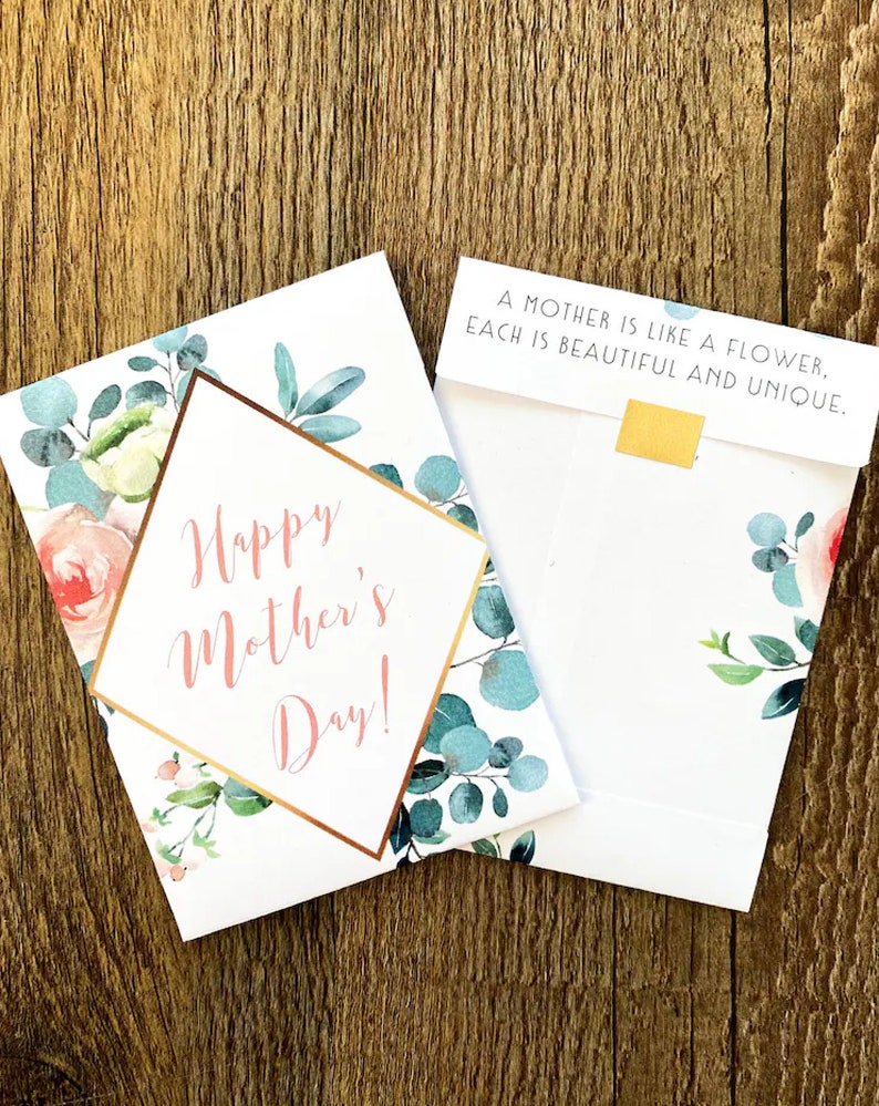 May include: Mother's Day greeting cards with floral designs. One card reads "Happy Mother's Day!" in pink script within a gold geometric frame. The other card reads "A mother is like a flower, each is beautiful and unique."