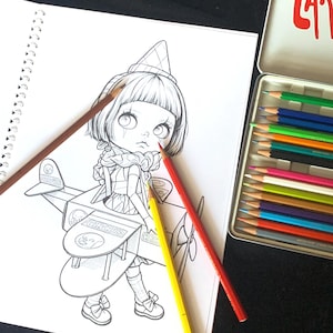 May include: A spiral-bound coloring book page featuring a line art illustration of a character in a cone hat sitting in a toy airplane labeled CIRCUS, accompanied by three colored pencils in red, yellow, and brown, and a metal tin of pencils.