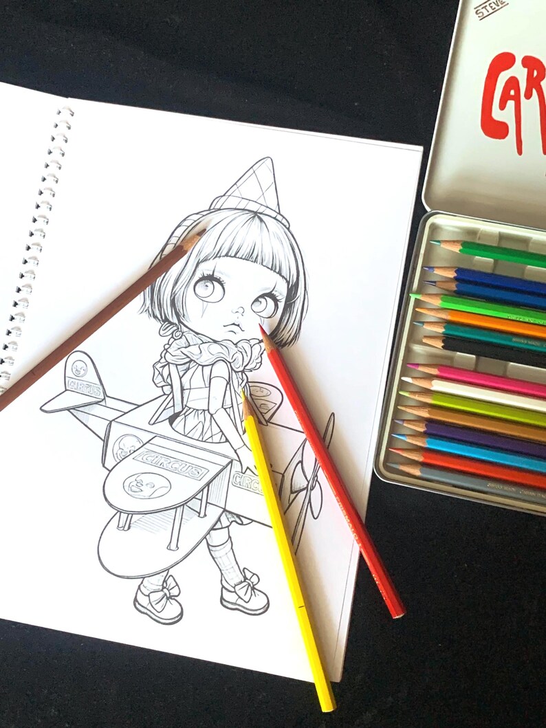 May include: A spiral-bound coloring book page featuring a line art illustration of a character in a cone hat sitting in a toy airplane labeled CIRCUS, accompanied by three colored pencils in red, yellow, and brown, and a metal tin of pencils.