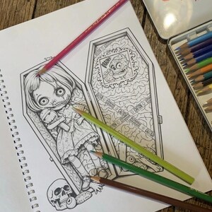 Peut inclure: Un dessin au trait noir et blanc dans un carnet &agrave; spirales repr&eacute;sentant une poup&eacute;e aux grands yeux tenant une plus petite poup&eacute;e dans un cercueil ouvert. Le couvercle du cercueil pr&eacute;sente une illustration de zombie avec le texte BRAINS et du ruban CAUTION. Des crayons de couleur sont pos&eacute;s sur la page.