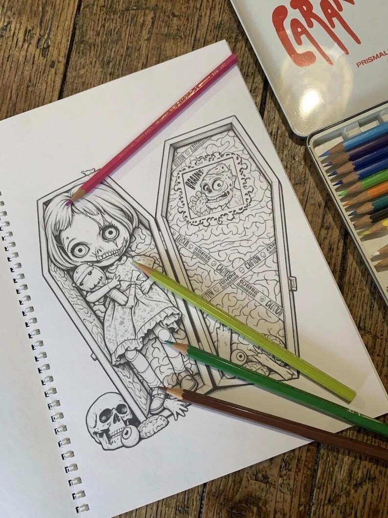 Peut inclure: Un dessin au trait noir et blanc dans un carnet &agrave; spirales repr&eacute;sentant une poup&eacute;e aux grands yeux tenant une plus petite poup&eacute;e dans un cercueil ouvert. Le couvercle du cercueil pr&eacute;sente une illustration de zombie avec le texte BRAINS et du ruban CAUTION. Des crayons de couleur sont pos&eacute;s sur la page.