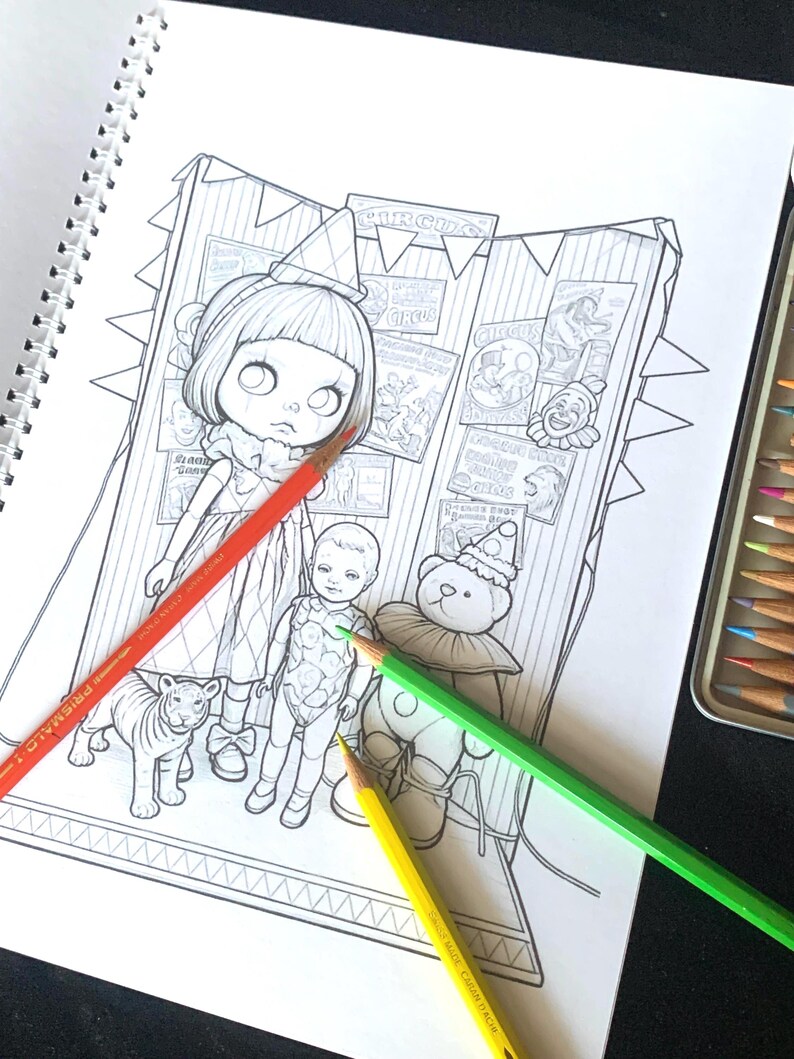 May include: A black and white coloring page featuring a girl in a party hat, a small doll, a tiger, and a teddy bear wearing a clown collar. The background shows circus posters and bunting. Three colored pencils in red, green, and yellow lie across.