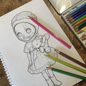 Peut inclure: Un dessin au trait noir et blanc sur une page de carnet &agrave; spirales repr&eacute;sentant une poup&eacute;e avec une coiffe en forme de cerveau, un visage squelettique et une robe, tenant un petit ours en peluche, accompagn&eacute; de quatre crayons de couleur.