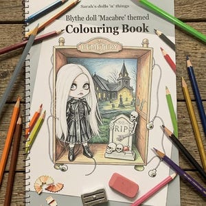 May include: A spiral-bound coloring book titled Sarah's dolls 'n' things Blythe doll 'Macabre' themed Colouring Book. The cover features a line art illustration of a doll with long hair standing in a cemetery scene with a tombstone and skeleton.