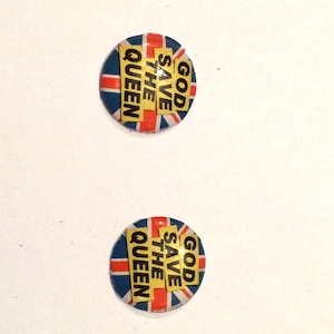 May include: Two round, blue, red and white button badges with a yellow background. The badges have the text "GOD SAVE THE QUEEN" on them.