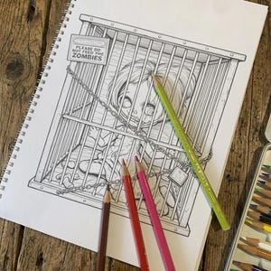 Peut inclure: Une page de cahier de coloriage &agrave; spirales pr&eacute;sentant une illustration au trait noir et blanc d'une poup&eacute;e enferm&eacute;e dans une cage en m&eacute;tal. Un panneau sur la cage indique WARNING PLEASE DO NOT FEED THE ZOMBIES. Trois crayons de couleur brun, rouge et rose.
