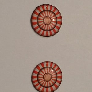 May include: Two round, red and white striped buttons with a concentric circle design. The buttons have a glossy finish.