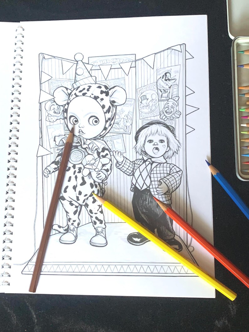 May include: A spiral-bound coloring book page featuring a black and white line art illustration of two circus-themed characters standing in front of a tent backdrop with posters. Three colored pencils in brown, yellow, and red rest on the page.